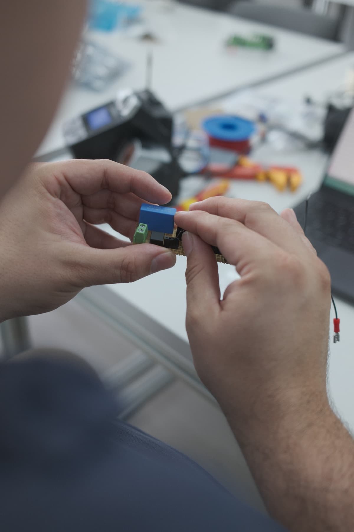 Mano sosteniendo un conector electrónico con el taller desenfocado al fondo